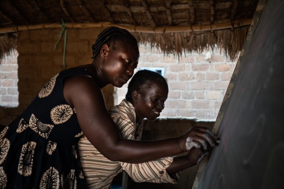 Afrikkalainen opettaja auttaa oppilastaan kirjoittamaan liitutaululle.