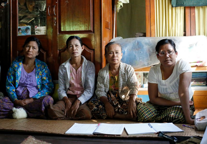 Neljä Myanmarin naisten ryhmän naista istuu pyödän takana. Pöydällä on papereita.