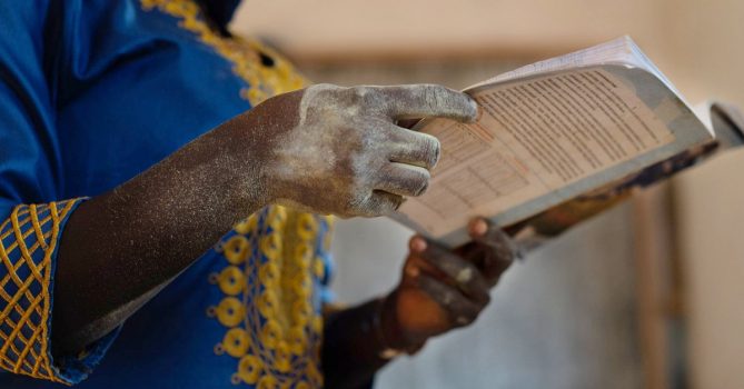 Afrikkalaisen naisen kädet pitelevät kirjaa.