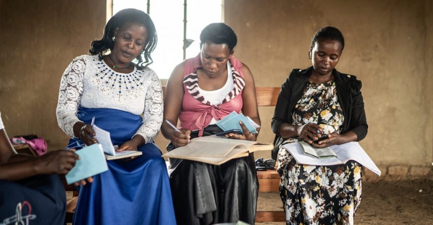 Kolme afrikkalaista naista istuu vierekkäin kirjoittaen lehtiöihin.