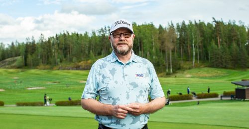 Mies lippalakkipäässä seisoo golfkentällä ja katsoo kameraan.