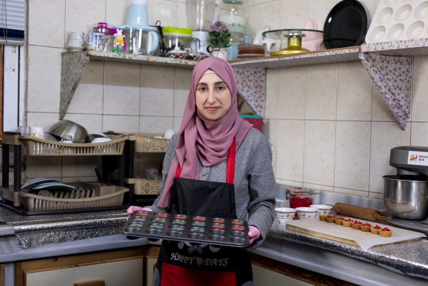 Esraa Al-Sehaiti seisoo keittiössä ja pitelee pellillistä herkkuja.
