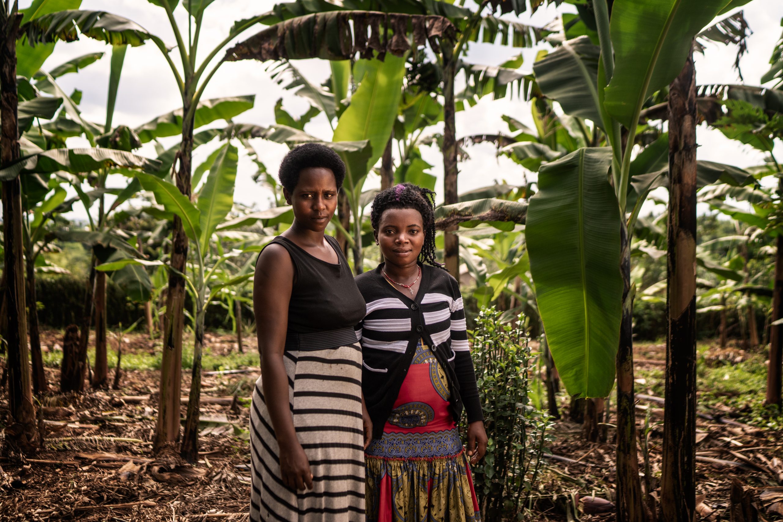 Kaksi naista seisovat verheän trooppisen viljelmän edessä.