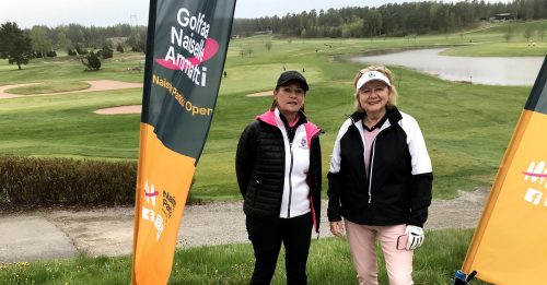 Kaksi naista seisoo esiteviirien välissä golfkentällä.