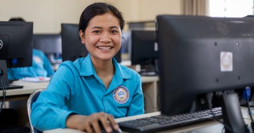 Nainen hymyilee tietokonenäytön takaa.