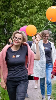 Naisia kävelemässä ulkona. Osalla on pinkkejä ja sinisiä ilmapalloja.