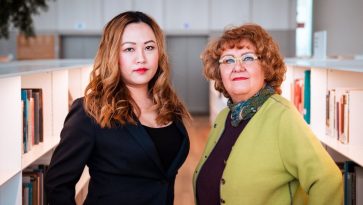 Kakasi naista seisoo kirjahyllyjen välissä.