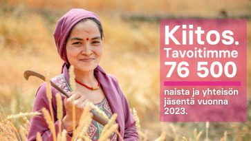 Nainen viljapellolla lila huivi päässään.