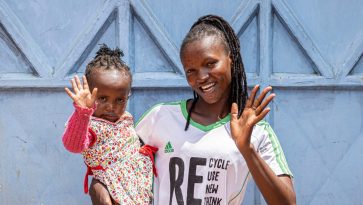 Nainen lapsi sylissä vilkuttaa.