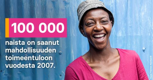 Nainen pinkissä paidassa ja hatussa hymyilee leveästi.
