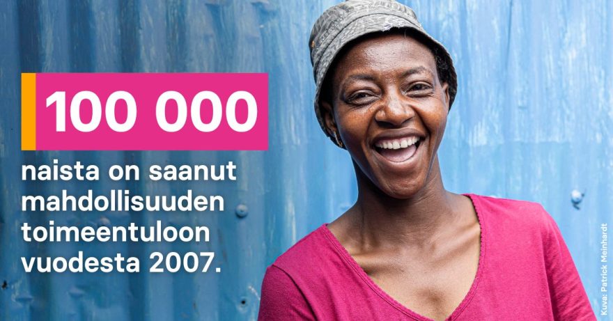 Nainen pinkissä paidassa ja hatussa hymyilee leveästi.