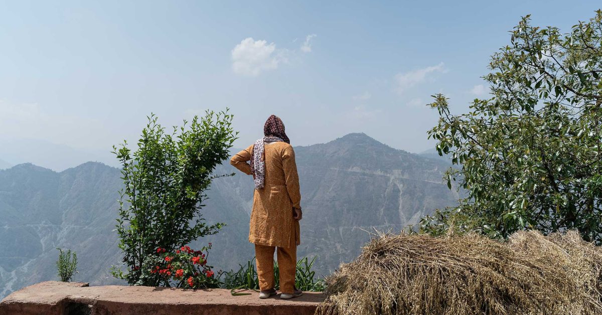 Nepalilainen nainen seisoo ulkona maaseudulla selin kameraan. Nainen katselee kaukaisuuteen, missä näkyy vuoria.