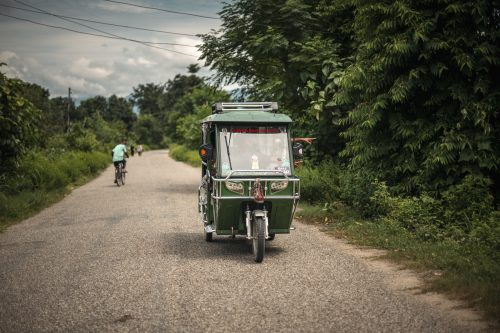 vihreä tuktuk-auto maantiellä vihreän metsän keskellä