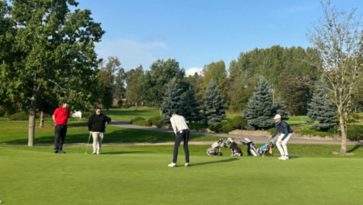 Kaksi ihmistä golfaamassa vihreällä kentällä.