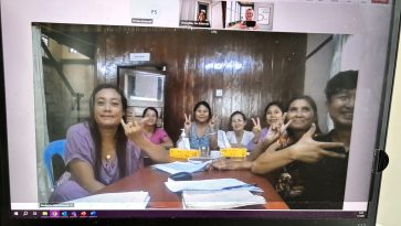 Kokoushuoneessa istuu ryhmä naisia näyttäen voitonmerkkejä.