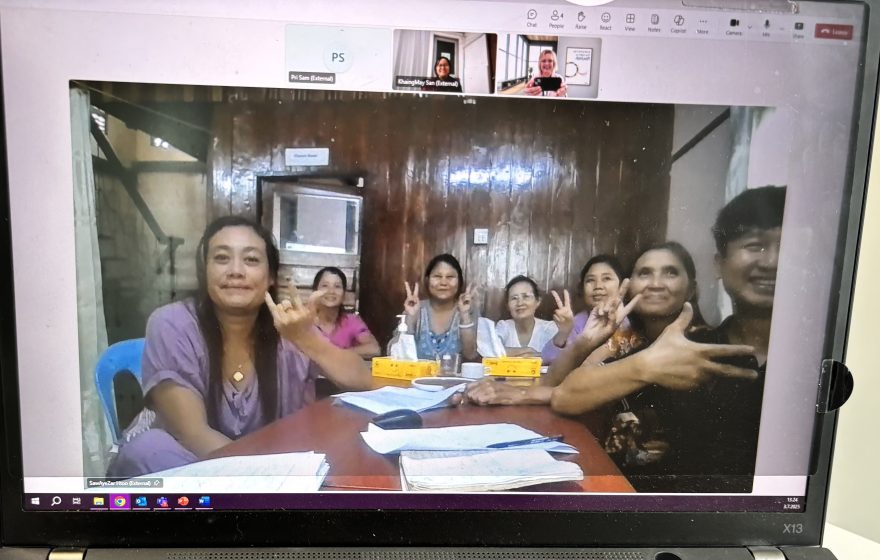 Kokoushuoneessa istuu ryhmä naisia näyttäen voitonmerkkejä.