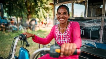 Nainen hymyilee tuk-tuk moottoriajoneuvon ratissa.