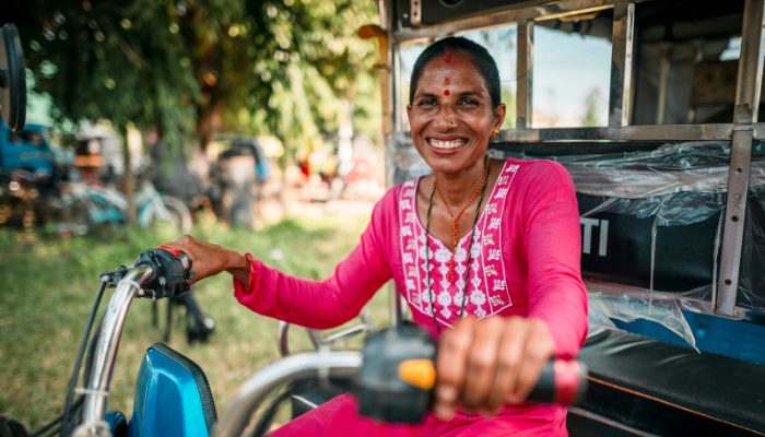 Nainen hymyilee tuk-tuk moottoriajoneuvon ratissa.