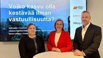 Kaksi naista ja mies seisovat pyöreän pöydän ääressä.