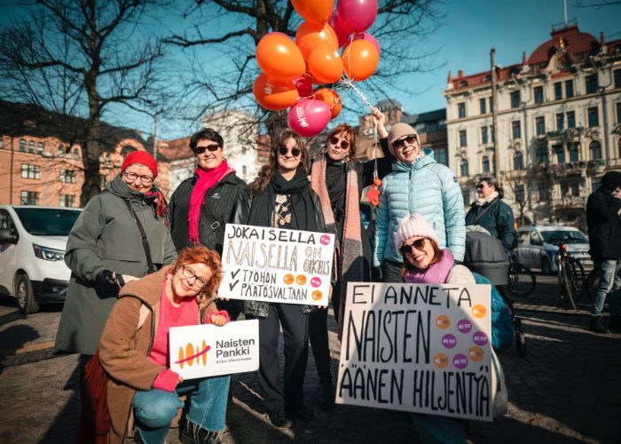 Joukko naisia pitelemässä tekstikylttejä ja ilmapallorykelmää.